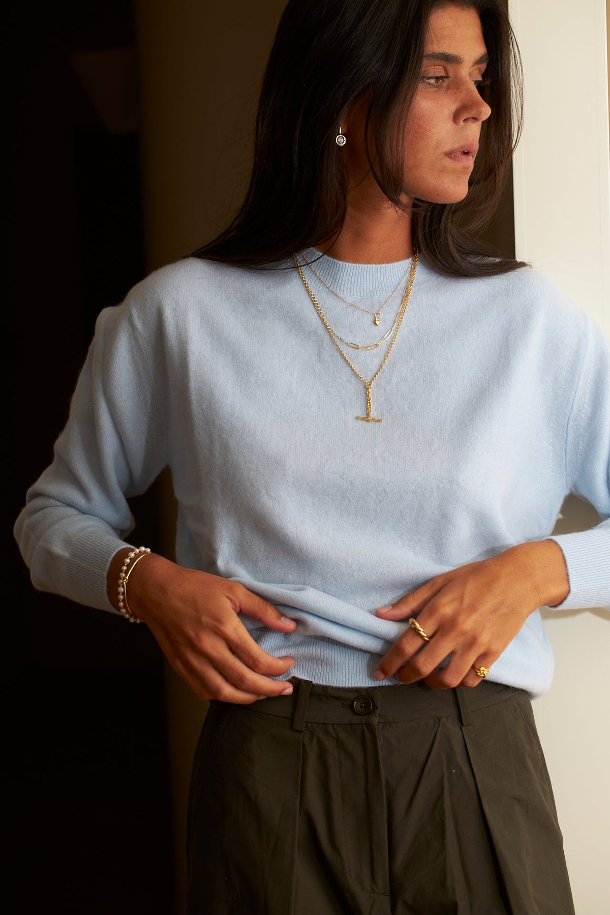 Necklaces for different necklines worn with a light blue sweater, showcasing layered gold jewelry styles.