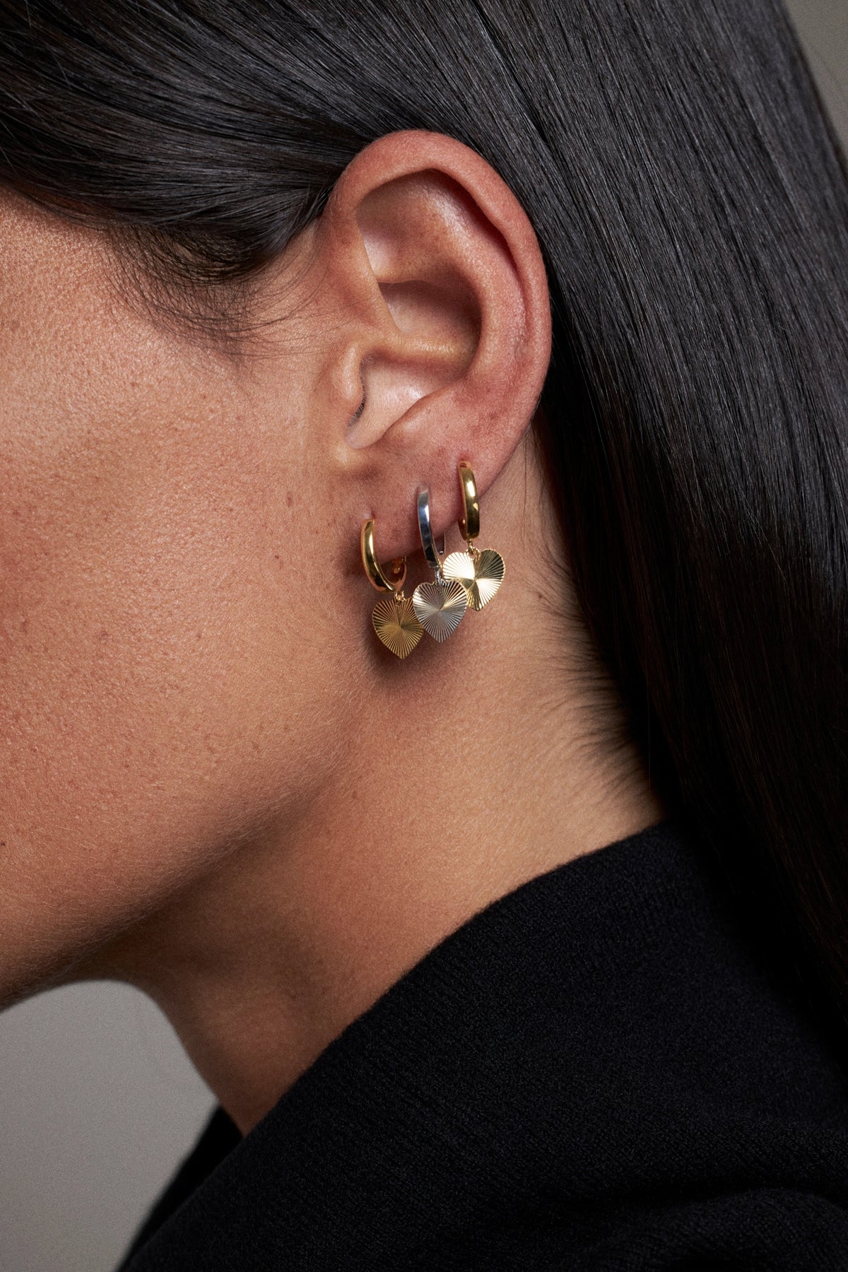 CINCO heart-shaped hoop earrings worn on ear, showcasing gold finish and colorful accents.