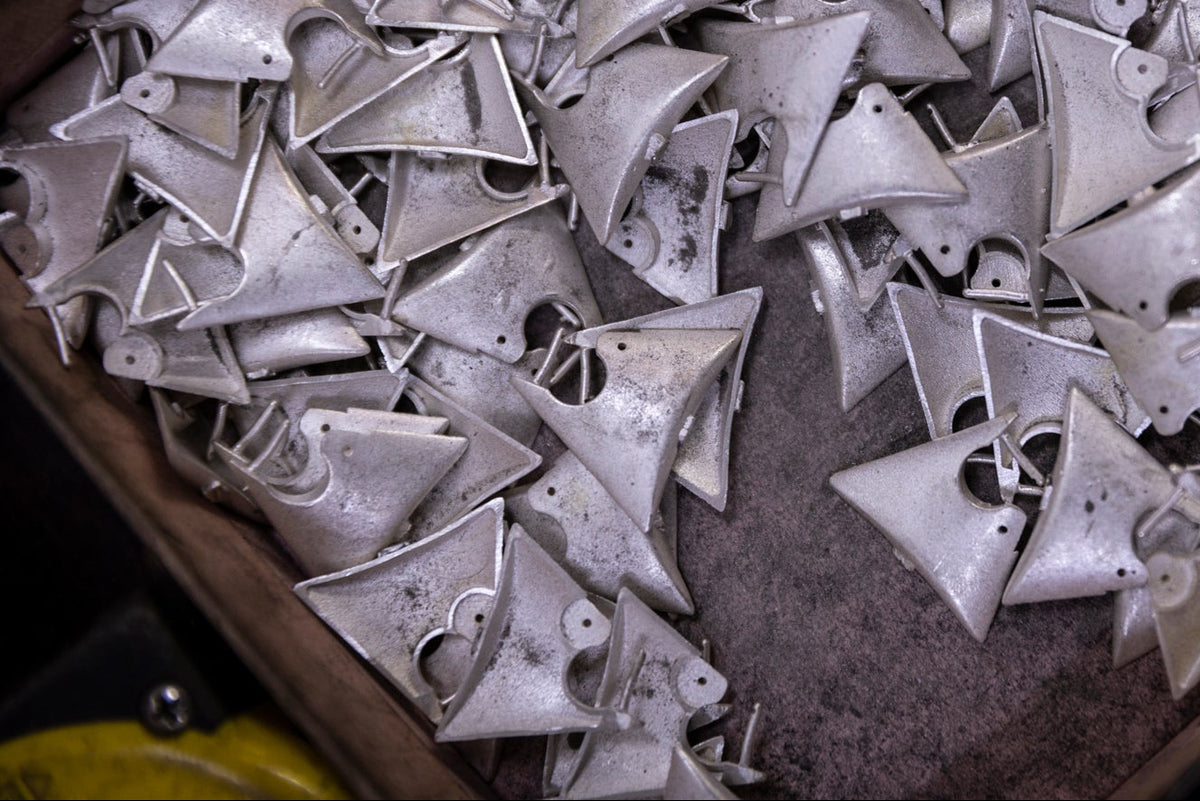A pile of small silver metal cone-shaped hardware pieces with circular cutouts, arranged inside a dark wooden tray or box.