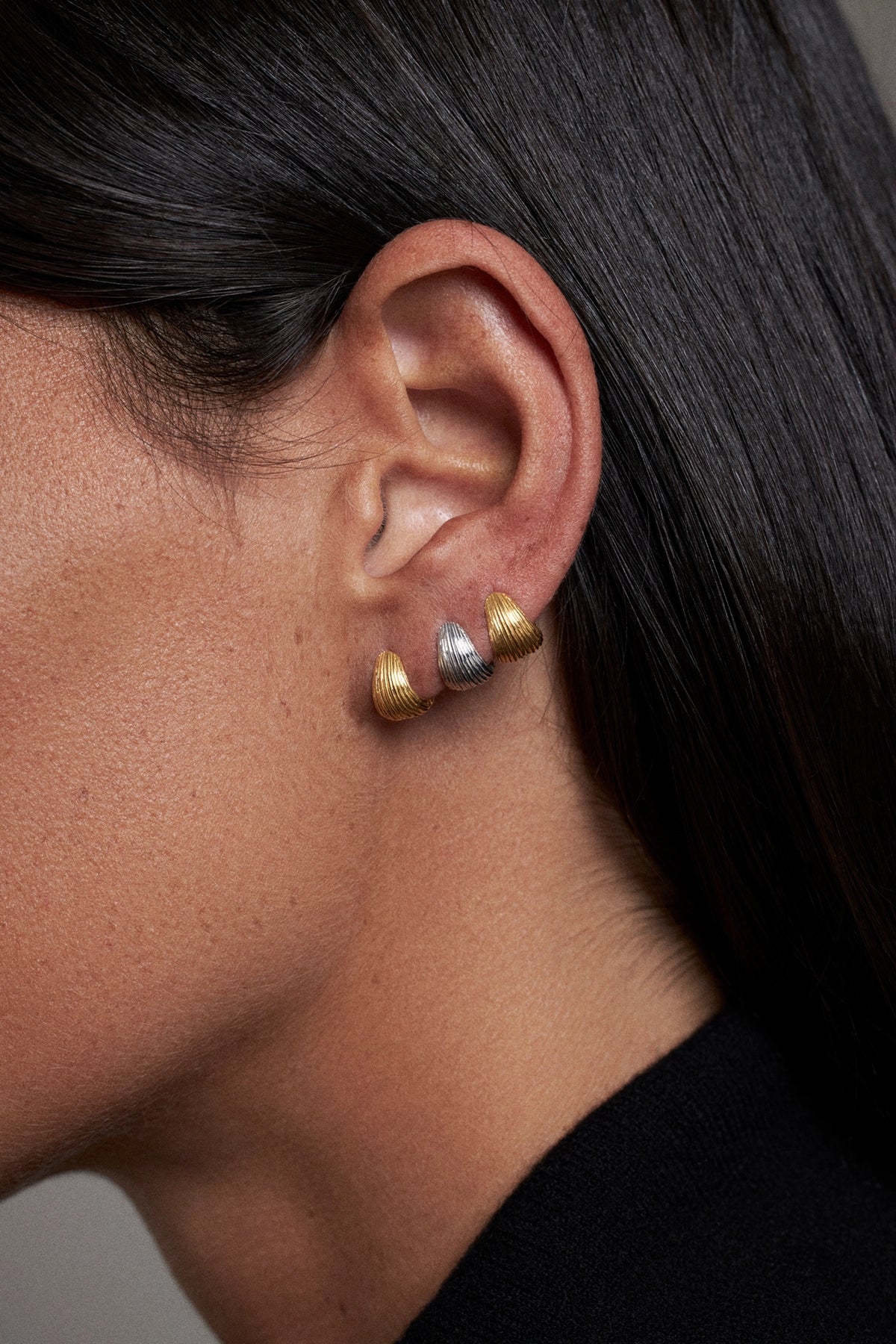 CINCO statement earrings worn on ear showcasing gold and silver colors in contemporary design.