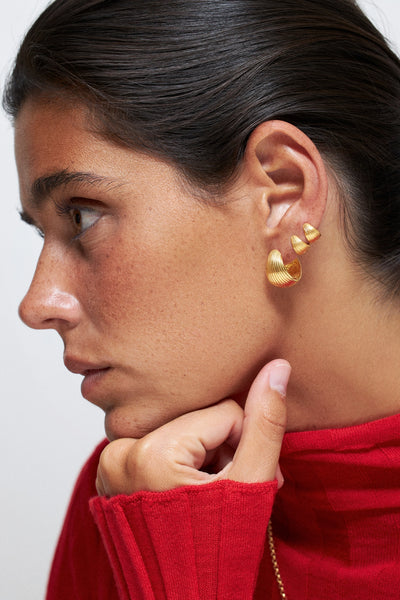 Tilly Huggie Earrings comfortable everyday wear present worn by a model with a red sweater, showcasing their elegant design.