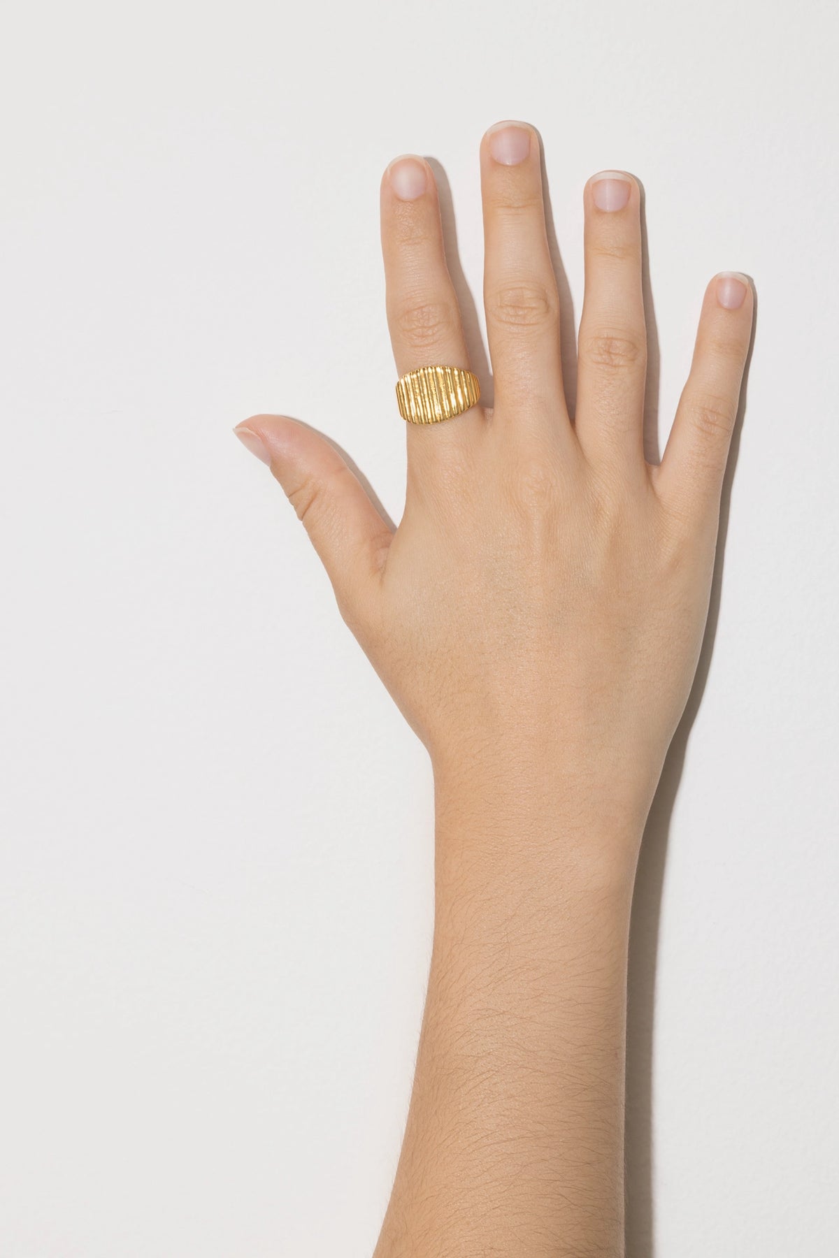 Textured fluted signet ring Cannelé in a hand on the index finger against a white background.
