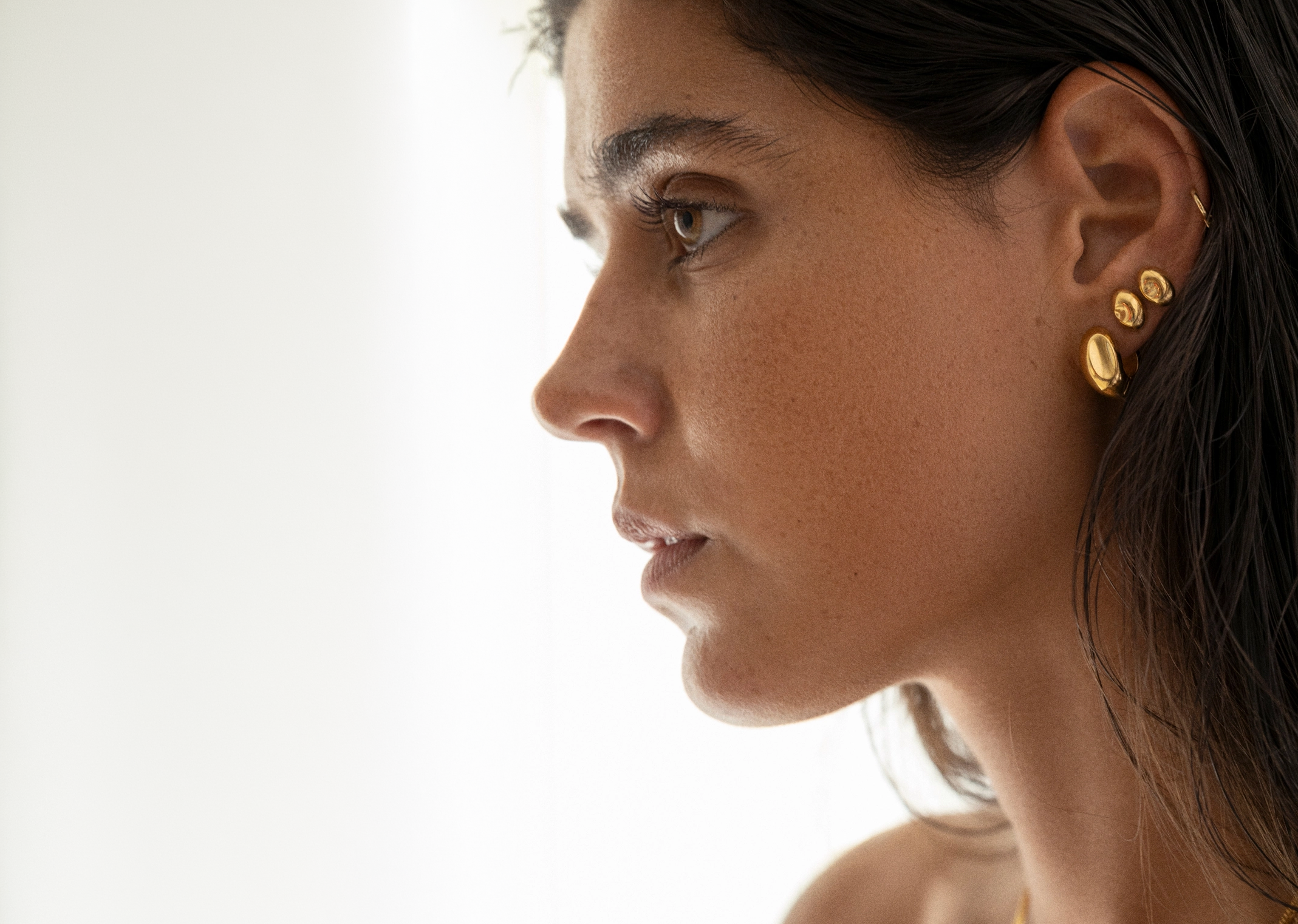 Close-up of a woman wearing gold earrings on a plain background